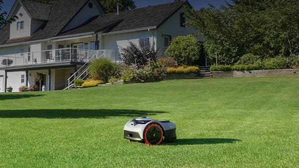 En modern, slinglös robotgräsklippare som automatiskt klipper en stor, välskött gräsmatta framför en vit villa.