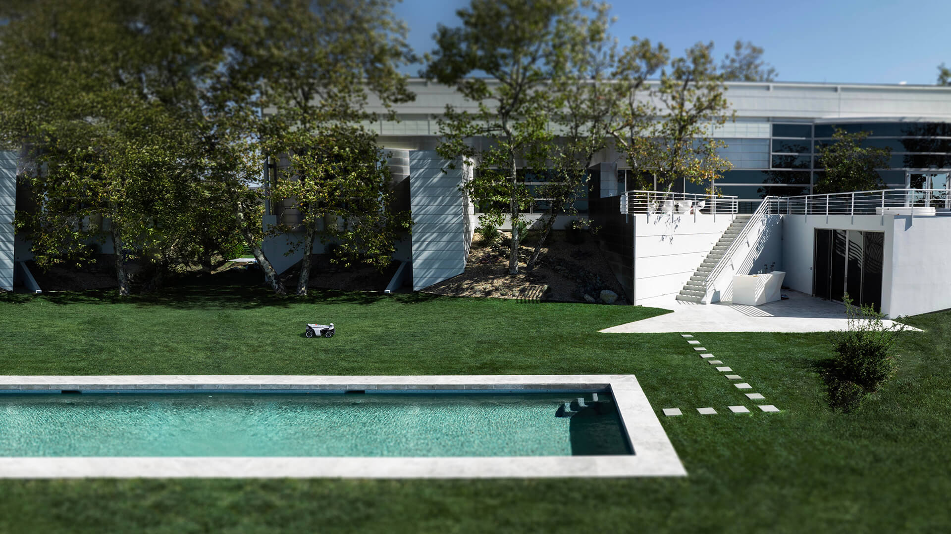 Modern robotgräsklippare som arbetar i en elegant trädgård med pool och modern villa.