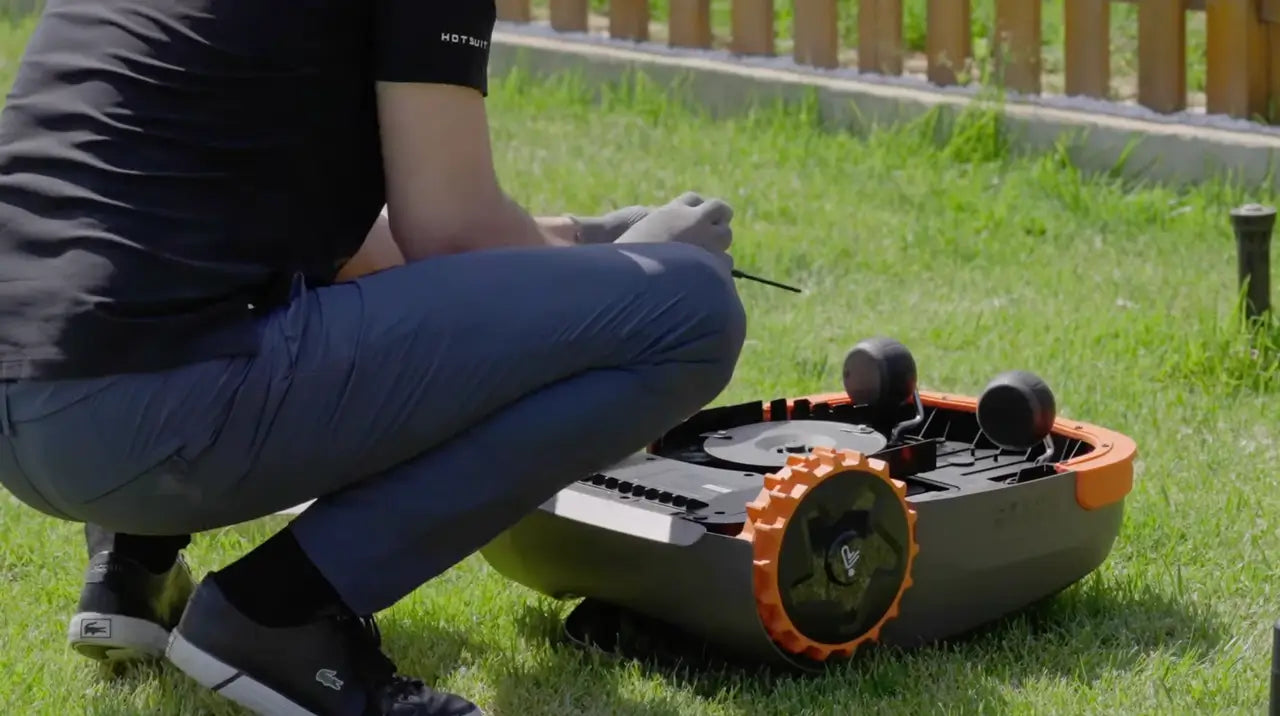 En person byter knivar på en robotgräsklippare i trädgården.