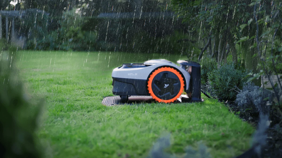 Robotgräsklippare som står vid sin laddstation på en gräsmatta under regn